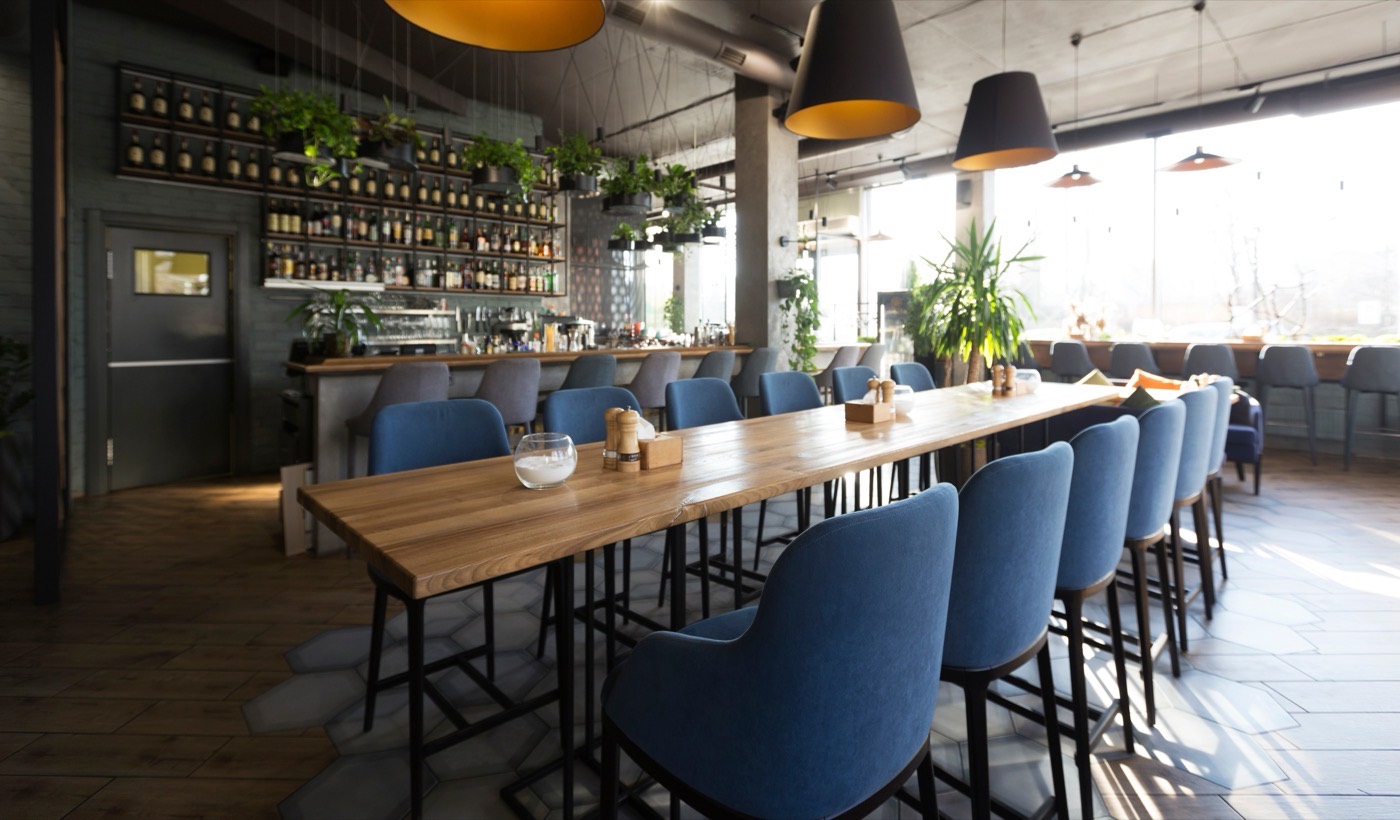 Inside a warm, modern restaurant — a long communal table beside the bar